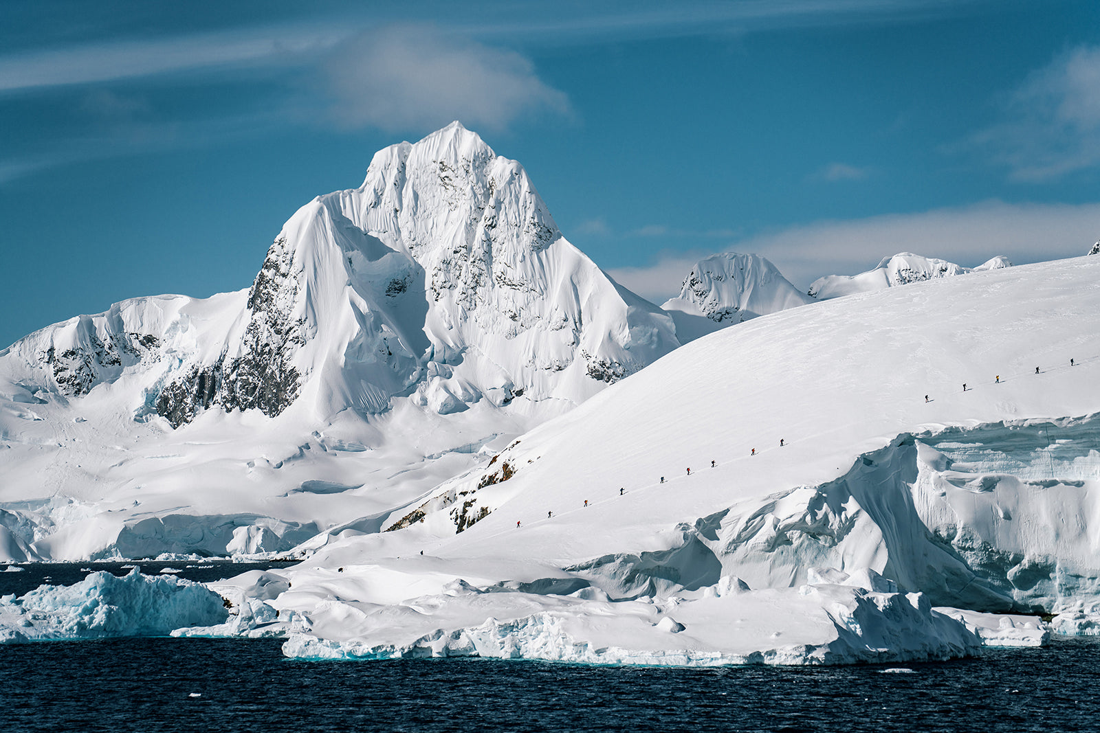 towering mountain backdrop with a long skin track of skiers touring up a glacier