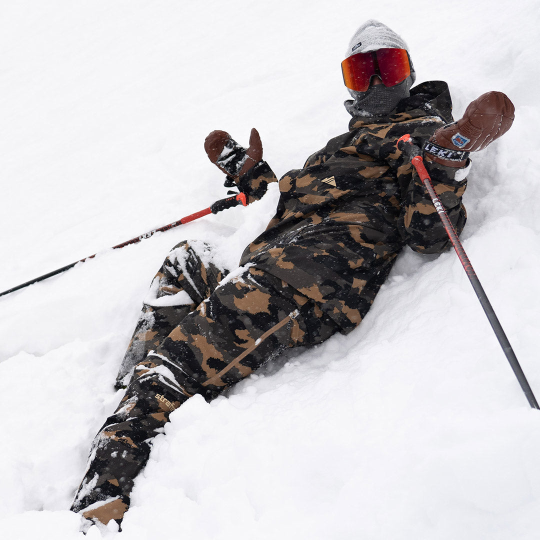 skier laying in snow in dune camo summit pant