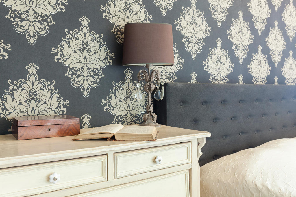 A close up pattern wallpaper of the bedroom behind of cream coloured cabinet with books and lamp