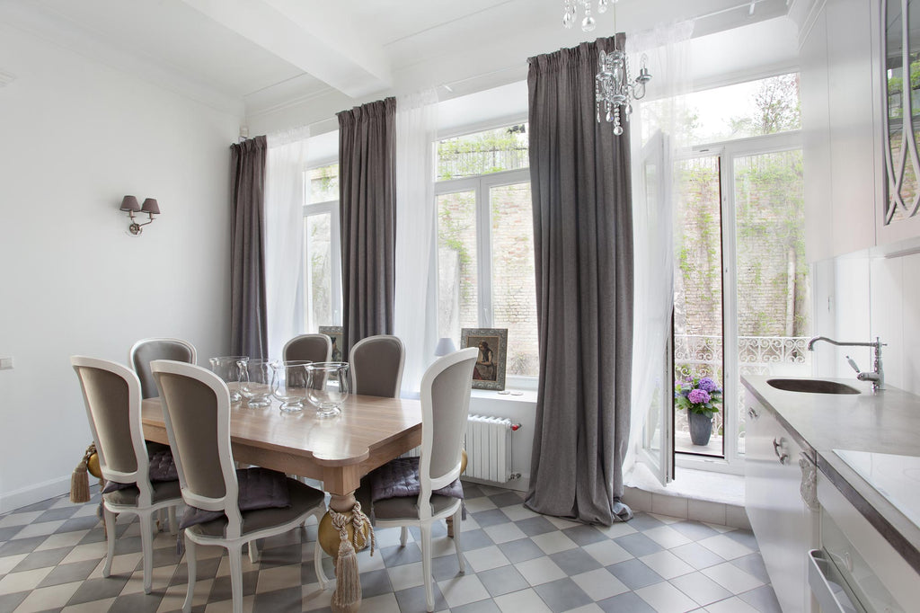 Beautiful dining room interior with long charcoal curtains from the top to bottom from the window and pattern square tiles on the floor under the family set dining table