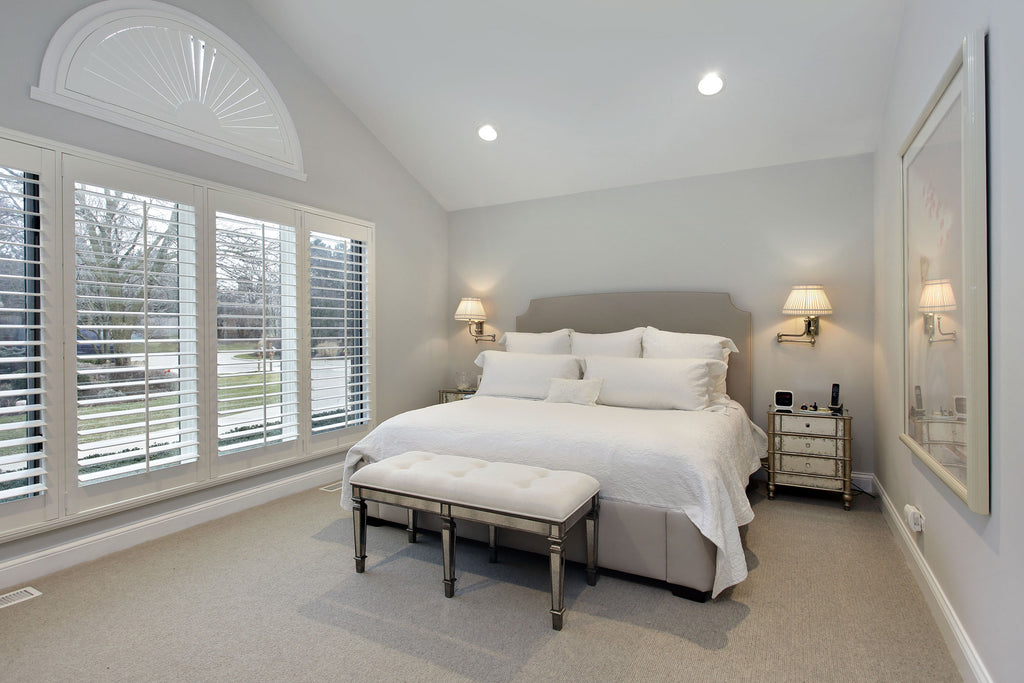 A modern bedroom interior with white wall and wooden shutters on the window with beautiful bedding with bench in the middle