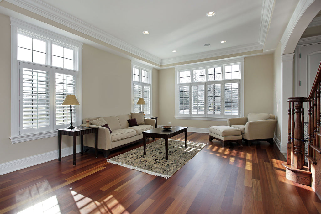 A modern living room in cream colour wall with the windows in wooden white shutters and wooden floors with cozy couch