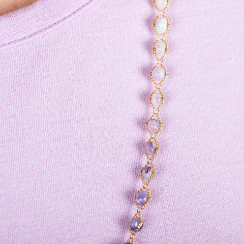 A close-up of an ombre amethyst beaded necklace woven through 18k yellow gold chain.