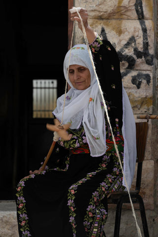 Near Hebron in the West Bank, a woman spins wool wearing a thoub decorated with tatreez. Image credit Annie O. Waterman.