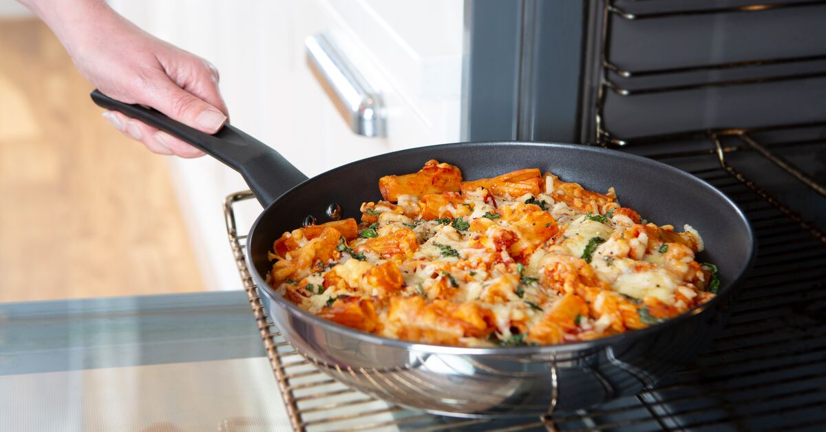 Cheesy pasta dish in frying pan being put into oven