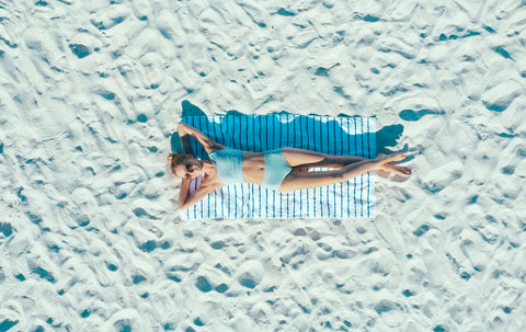 Woman laying on a big sandy beach wearing The Base Foundation