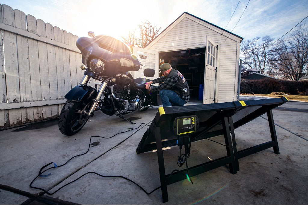 Man repairing motorcycle with power station and solar panel setup