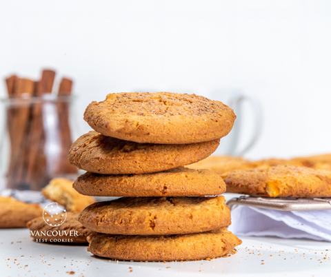 a pile of ginger cookies in the front with a glass jar filled with cinnamon sticks in the background