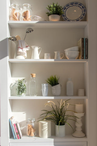 Bibliothèque blanche avec décoration, plantes, livres et bougies.