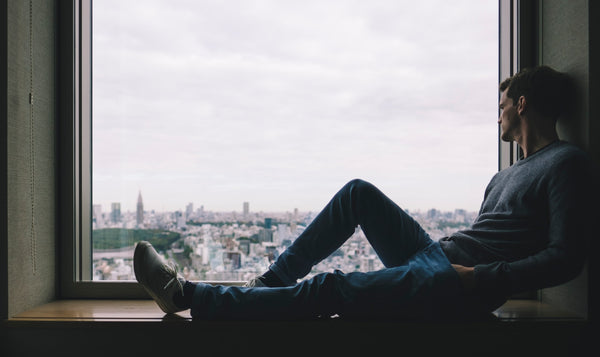 Chronic loneliness: person sits alone on a windowsill and looks out