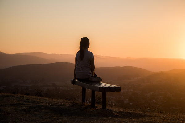 Person sits on a bench at sunset and looks out at the landscape