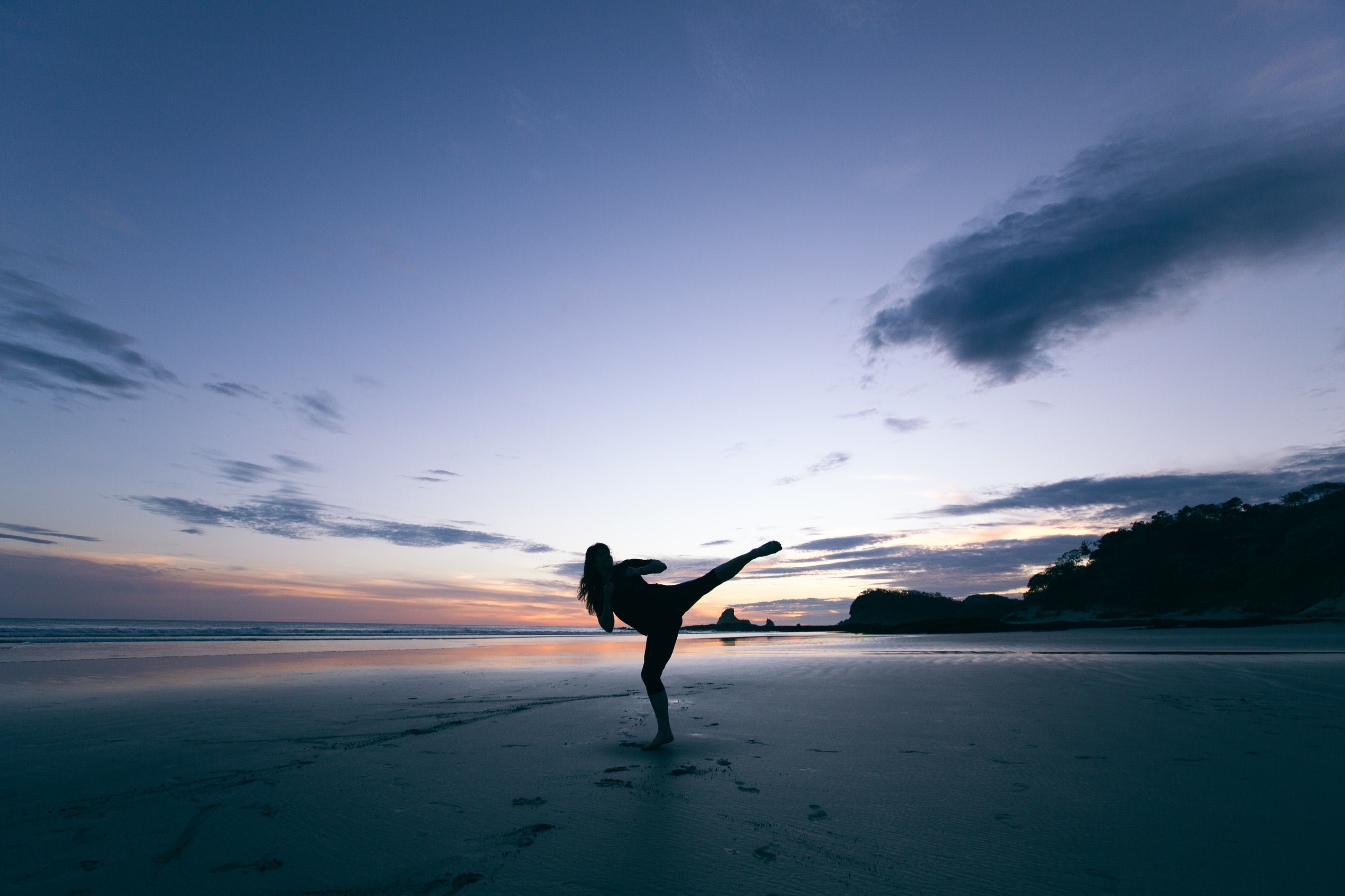 Person is in fighting pose on a beach at sunset