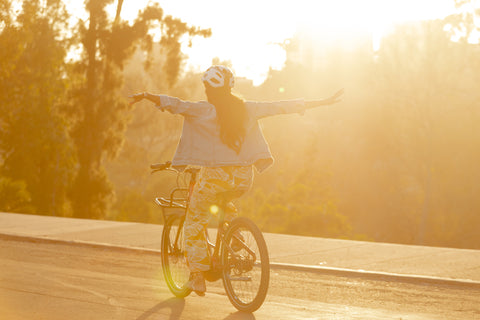 Woman riding bike with no hands at sunset.