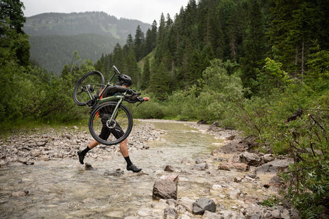 GRAVEL BIKER CROSSING RIVER CARRYING BIKE