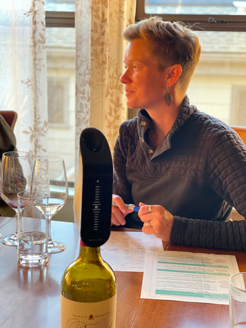 Image of the Aveine aerator and wine glasses on a table, with a woman in the background