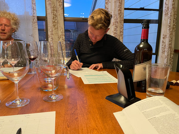 Reviewing the impact of the Aveine wine aerator. Image pictures a woman writing on a worksheet with a bottle of wine and wine glasses in the foreground.