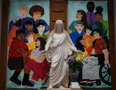 two art quilts featuring people of many ethnic backgrounds behind a marble statue of Jesus