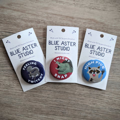 A collection of wildlife themed buttons. The first has an illustration of a squirrel with the words "Feeling Twitchy." The second is an illustration of a snapping turtle with the words "I Might Snap." And the third is an illustration of a raccoon with its hand up and the words "High Five."
