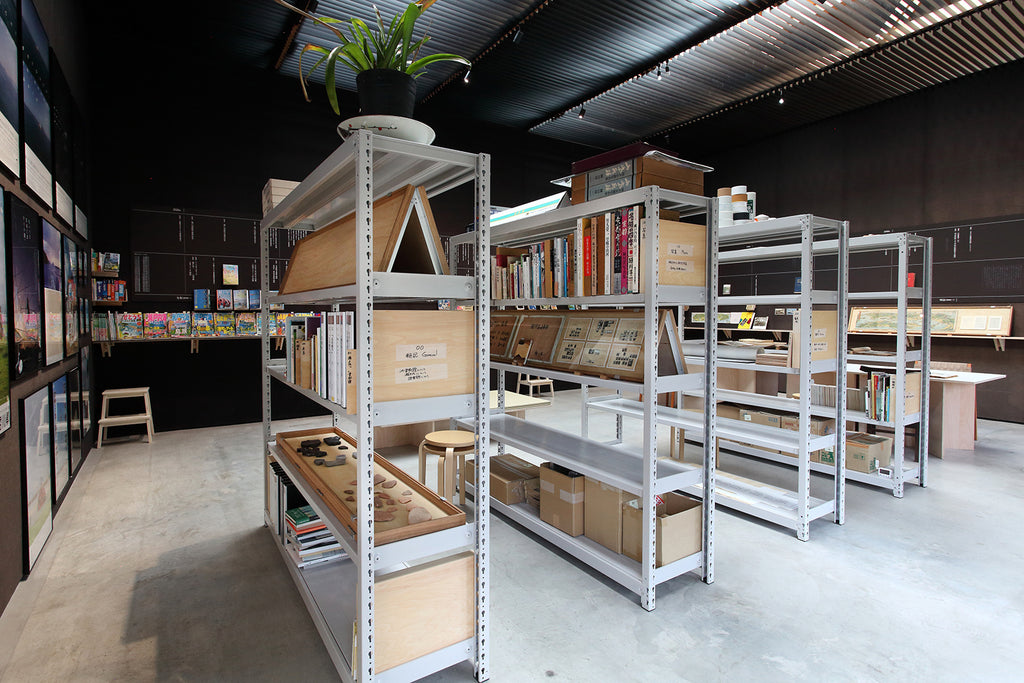 Four industrial bookshelves form the core of the archive. Rather than live behind the scenes, they are the dominant visual element in the gallery space. Photo courtesy of Motoyuki Shitamichi.