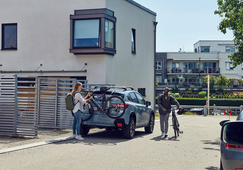 A man and a woman standing next to their car with a Thule Outway 3 bike rack attached