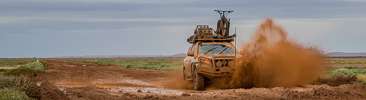 A muddy 4WD Toyota Landcruiser driving through the Australian outback