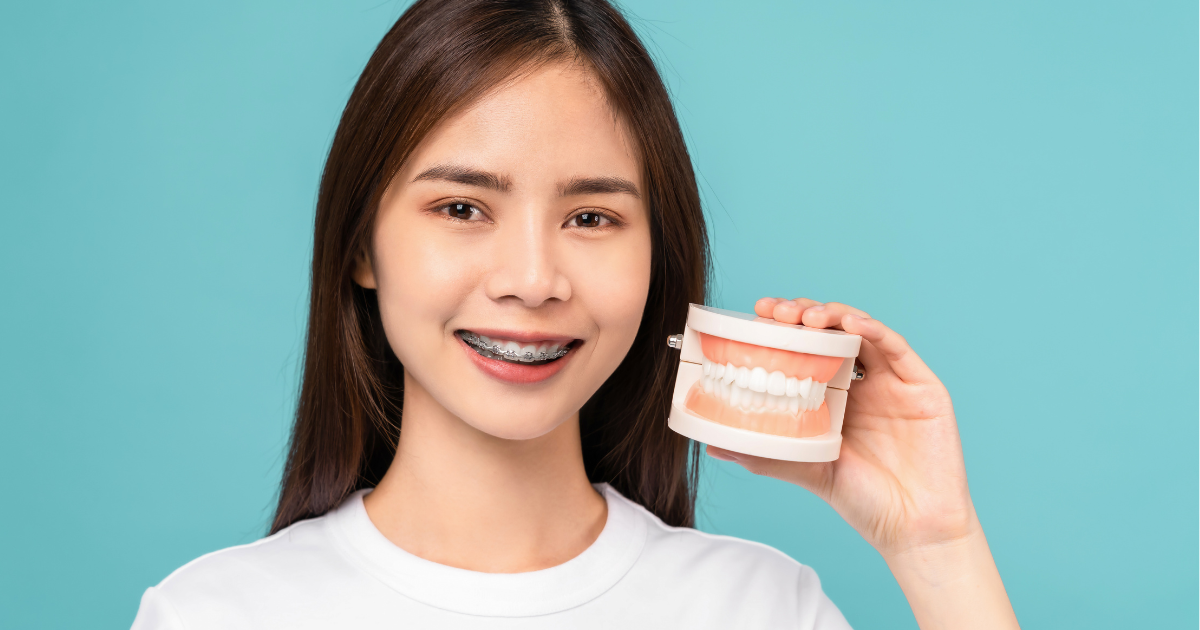 A close-up view of a person's healthy teeth while holding a denture in a blue background