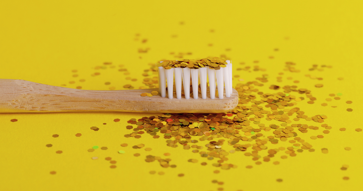 A bamboo toothbrush with a bunch of glitter on top of it bristle in a yellow background