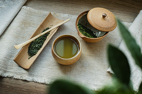 A cup of green tea alongside a container of dried green tea leaves