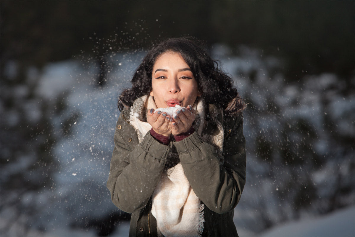 A woman blowing snow out of her hands