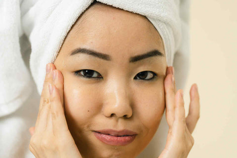 A young Asian woman wearing a white hair towel and touching her face