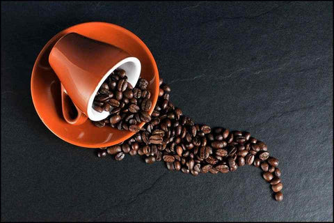 A tilted orange cup on a saucer spilling coffee beans