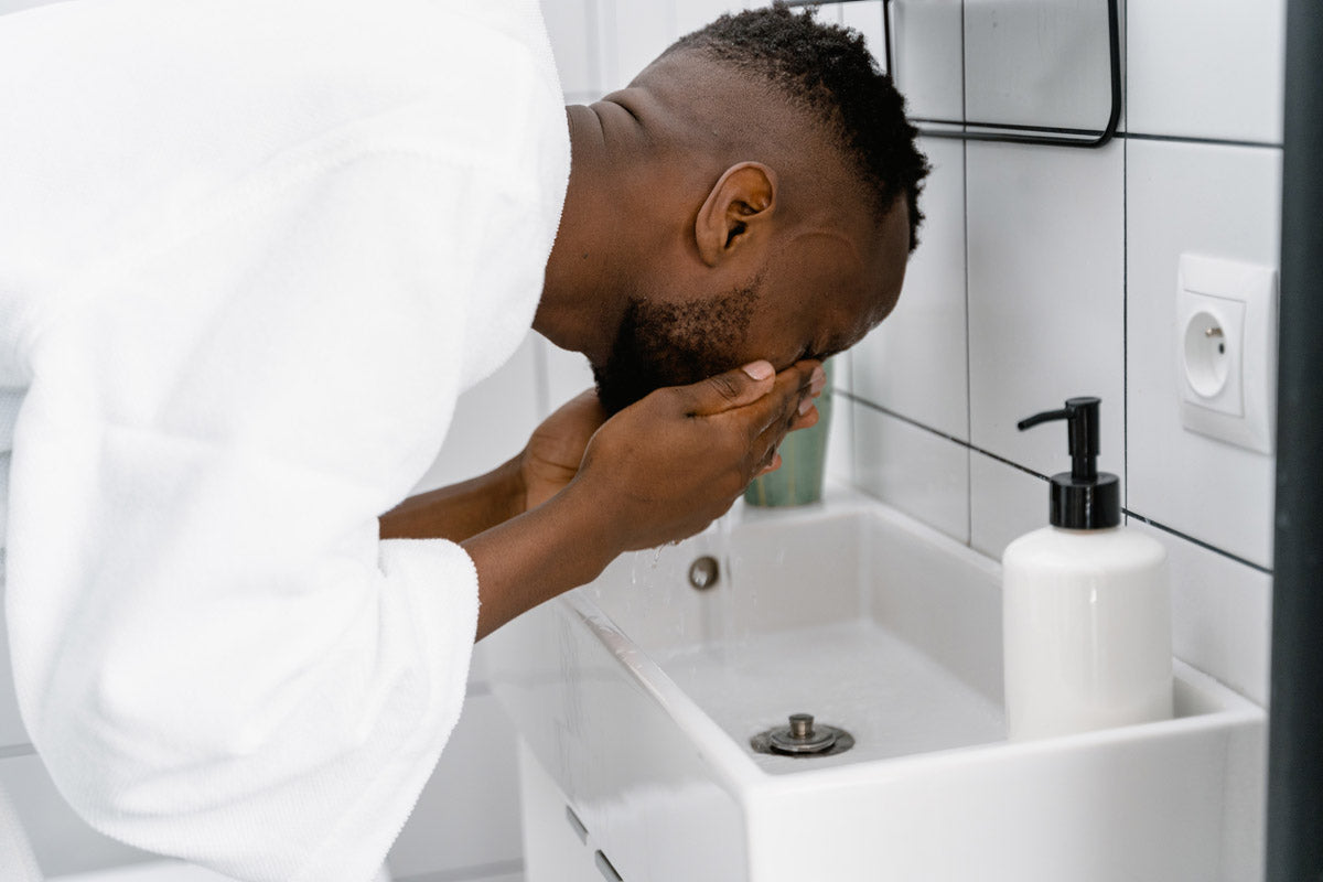 A man washing his face in a white robe and white bathroom