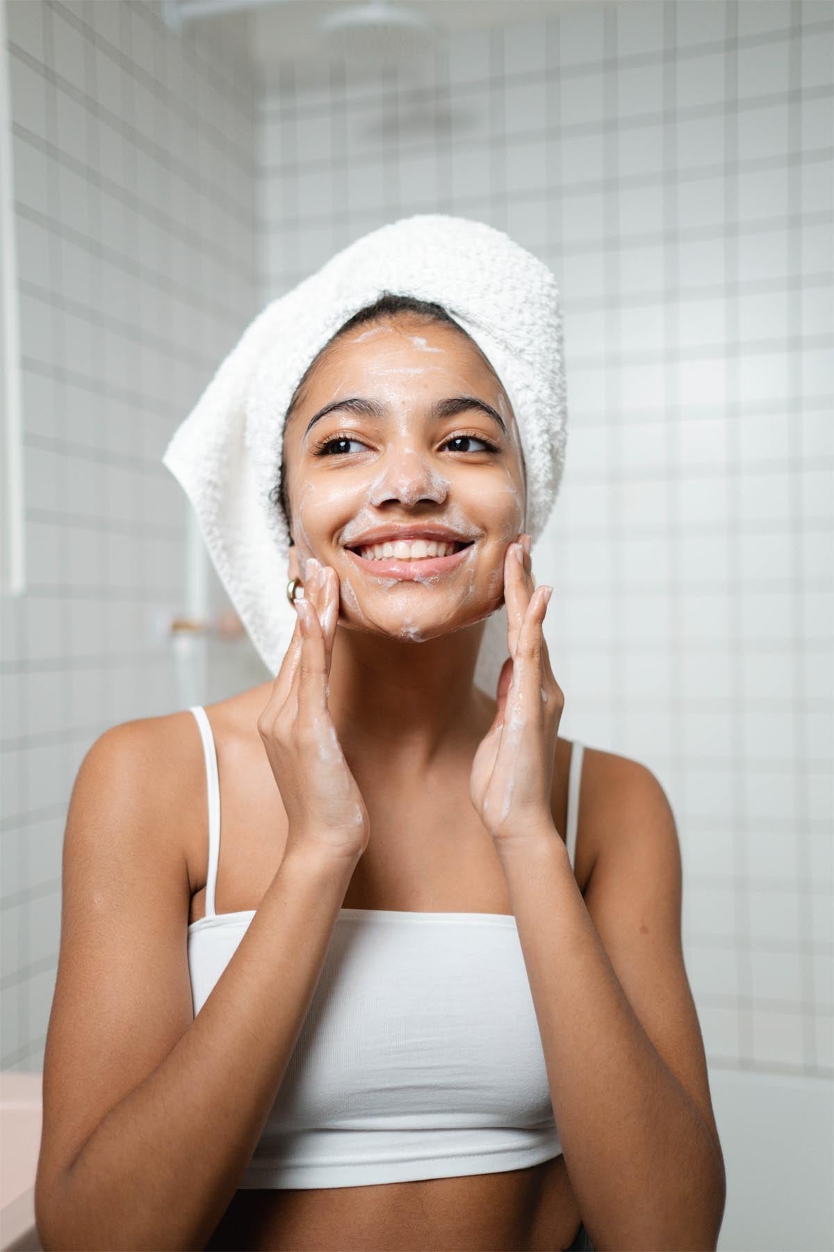 a woman cleansing her skin with a white towel on her head
