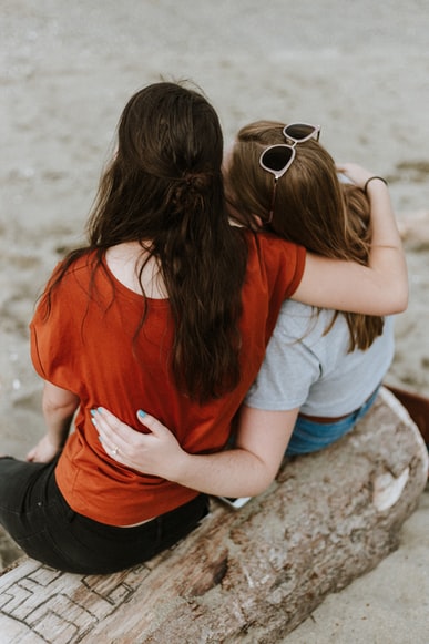 women sitting on a log with their arms wrapped around each other