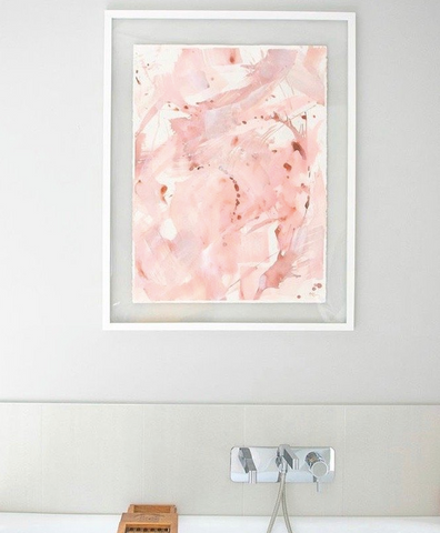 An abstract pink artwork in a white floating frame installed in a minimalist bathroom
