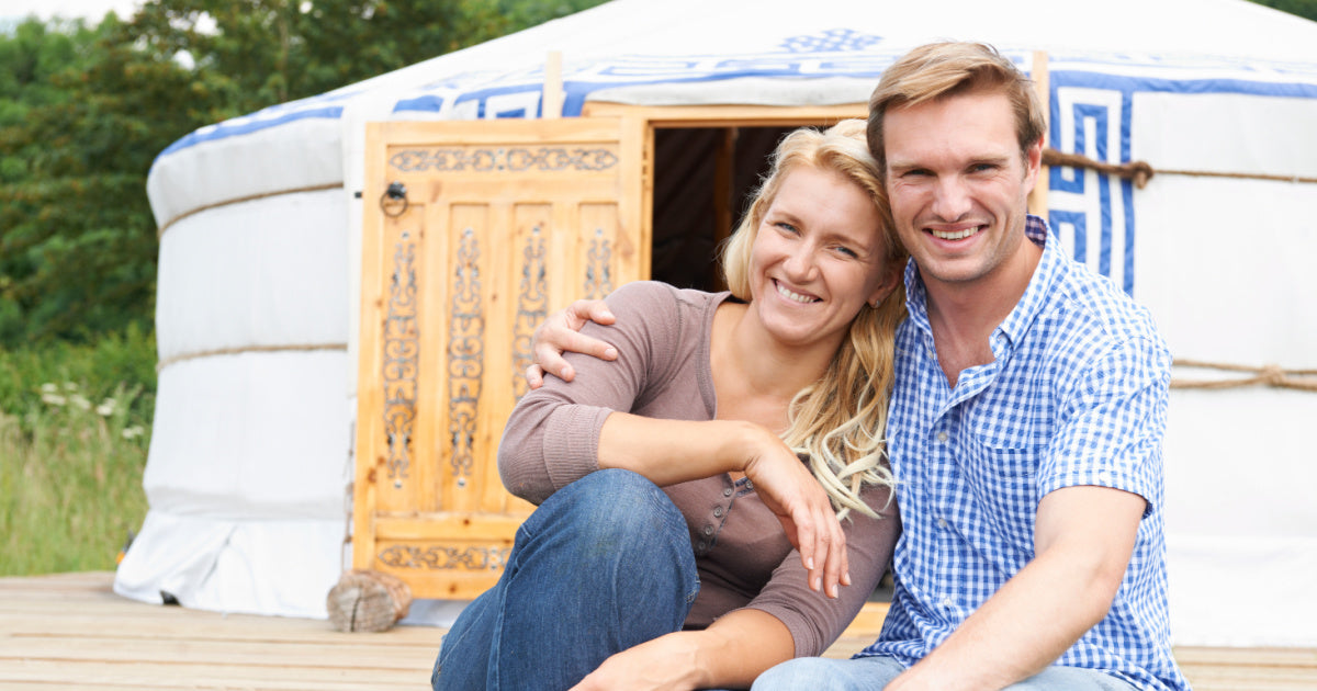 smiling couple sitting in a wooden deck in front of a yurt