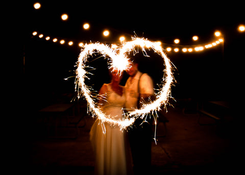 married couple at wedding kissing behind a heart made by a sparkler