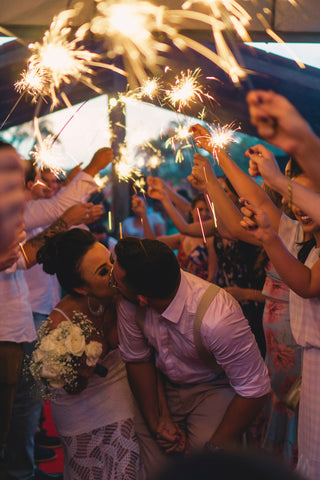 newly married couple kissing under sparklers held by guests