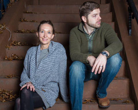 An image of a woman and man in their 30s  at night sitting on a brown stoop in Brooklyn.
