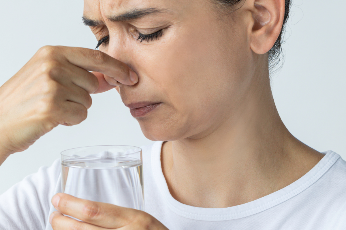 woman holding a glass of water plugging her nose