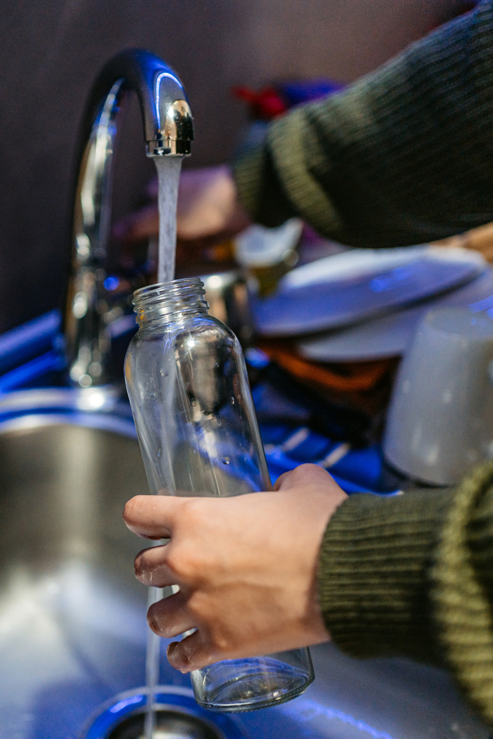 person filling glass water bottle with water