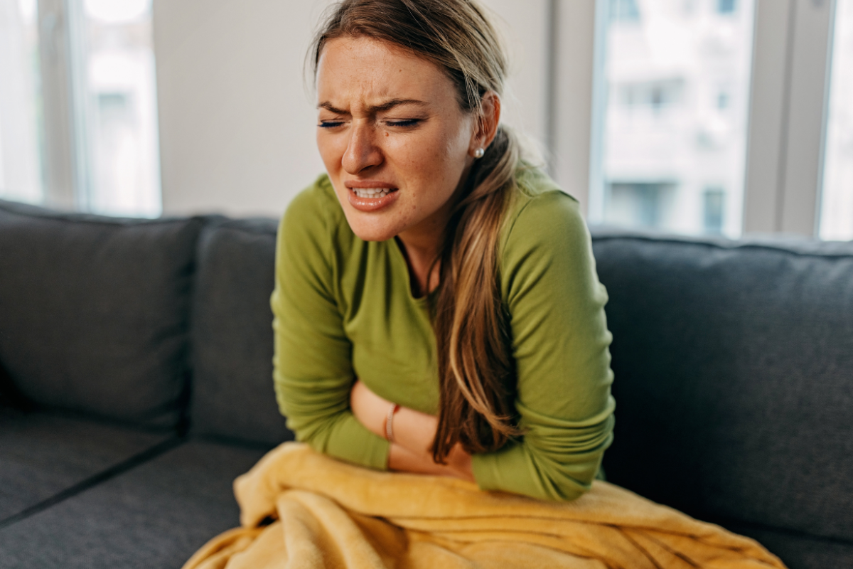 a woman sitting on a couch with stomach pain holding her stomach