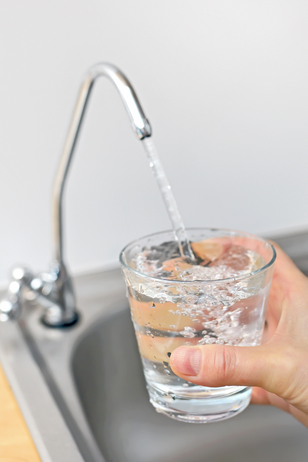 person filling glass of water from sink faucet