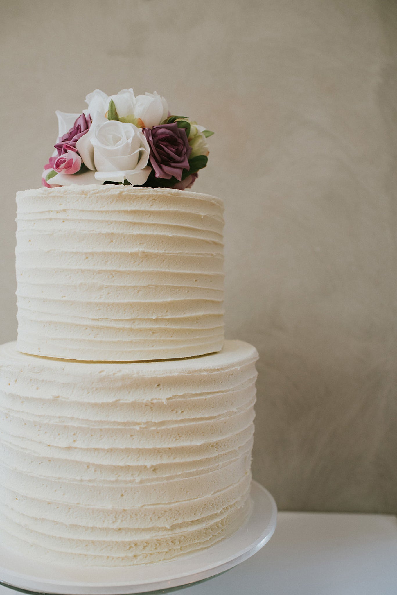 two tier wedding cake with flower topper in pink purple and cream