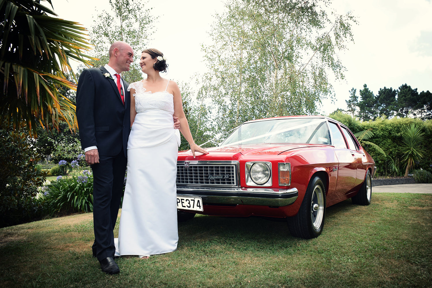 bride and groom standing in front of a vintage red Holden Kingswood