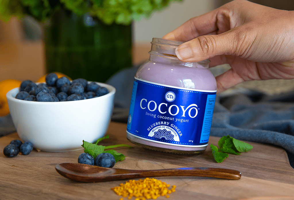 Woman holding jar of GT's COCOYO Blueberry Ginger and bowl of blueberries