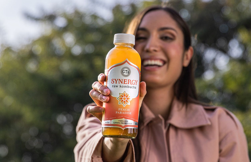 Woman smiling with GT's SYNERGY Peach Paradise Raw Kombucha