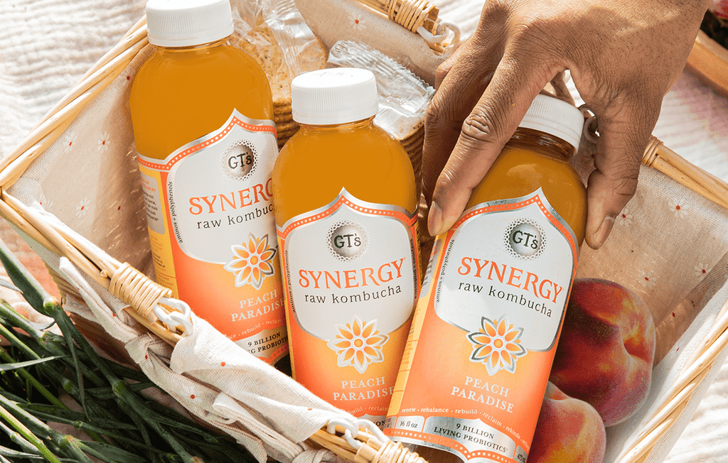 GT's SYNERGY Raw Kombucha Peach Paradise in basket with hand