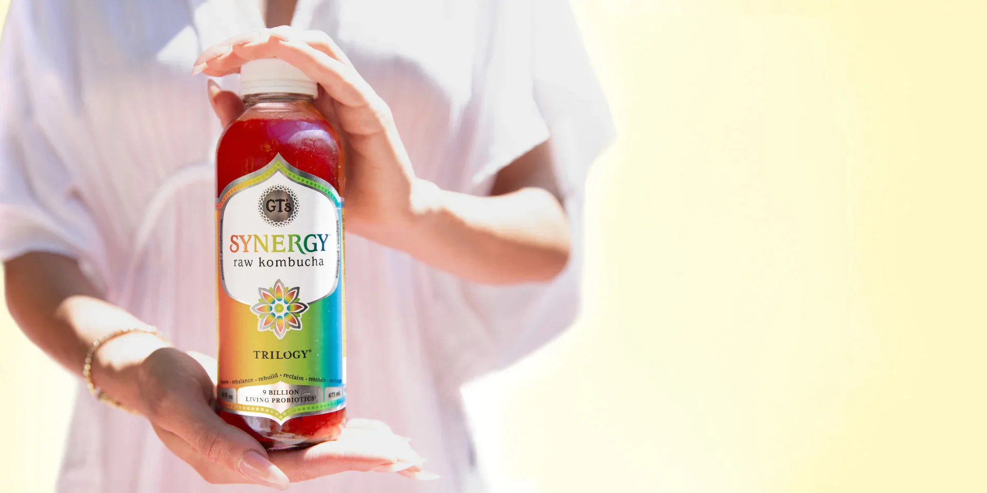 Woman holding a bottle of SYNERGY Trilogy Raw Kombucha