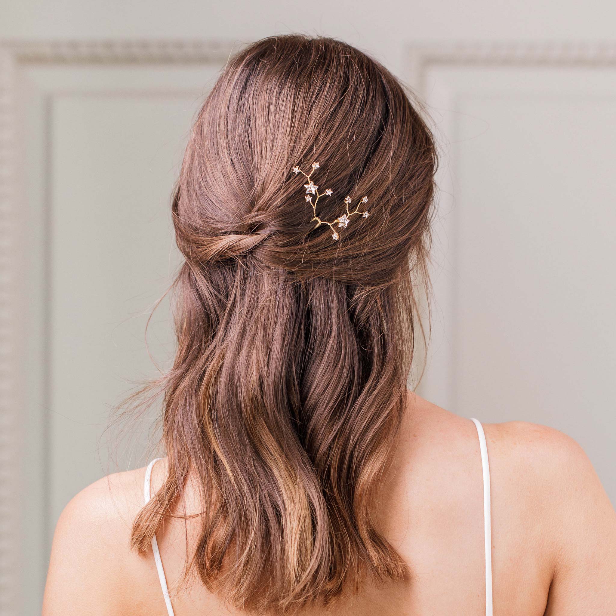 The back of a womans head with soft brown curls. In her hair there is a gold and crystal hair pin